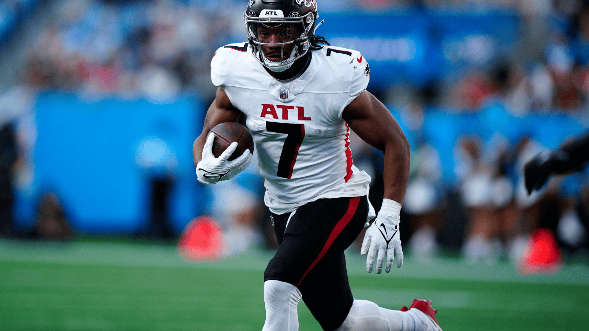 bijan robinson, in a white jersey with atl and the number 7, sprints down a football field, holding the ball, with a determined expression