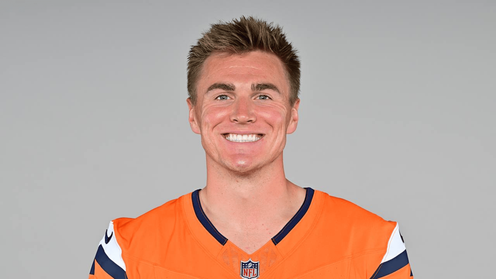 bo nix wearing an orange sports jersey with dark blue and white accents smiles at the camera against a neutral background conveying a cheerful mood