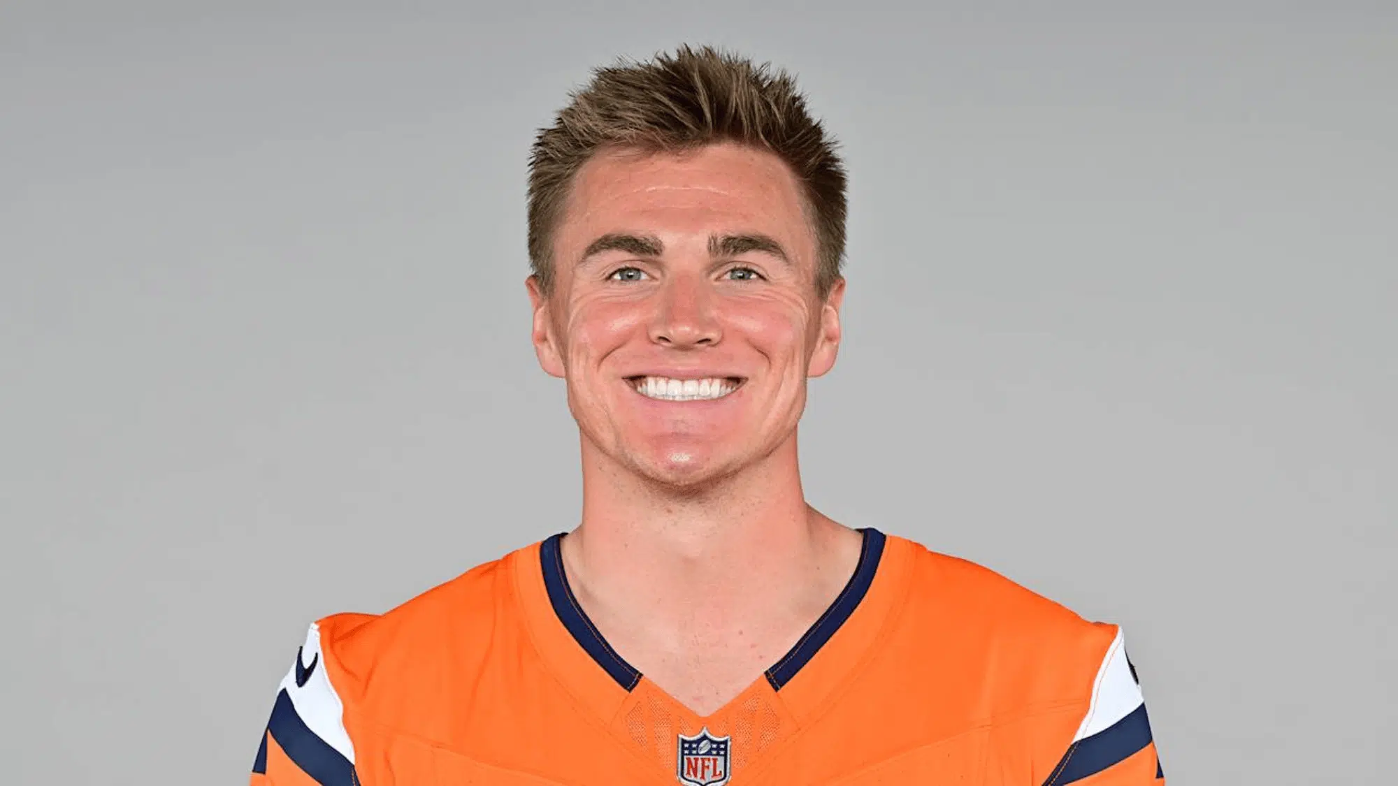 bo nix wearing an orange sports jersey with dark blue and white accents smiles at the camera against a neutral background conveying a cheerful mood