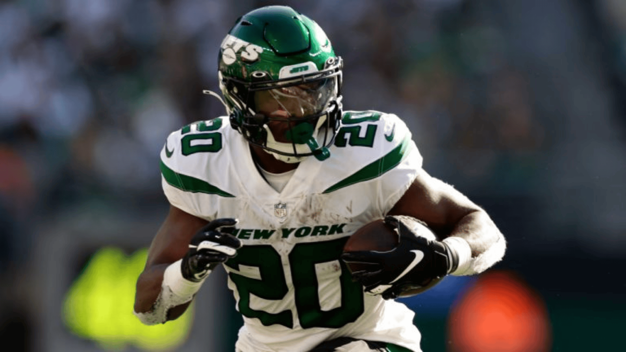 breece hall in a white and green new york jets uniform is running with the ball
