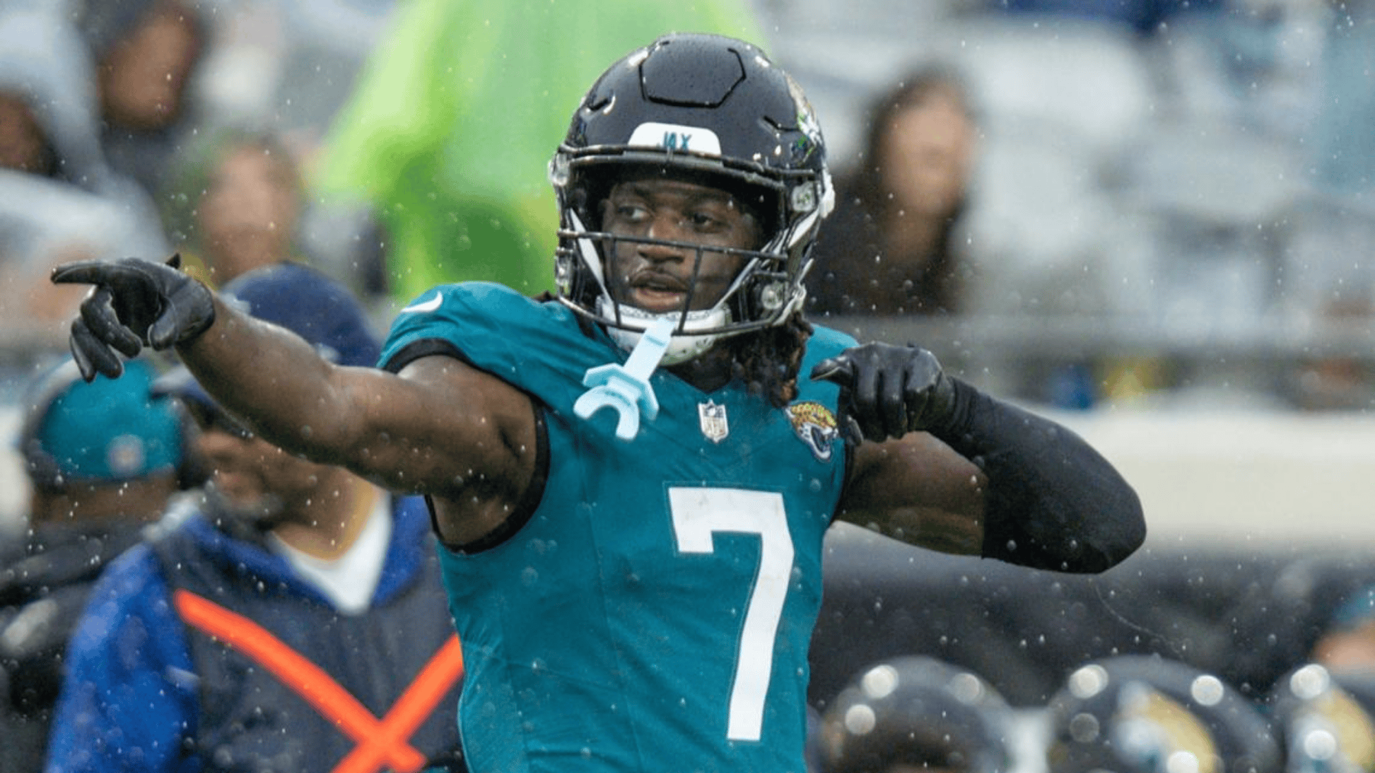 brian thomas jr. in a teal jersey number 7 points into the distance amid rainy weather