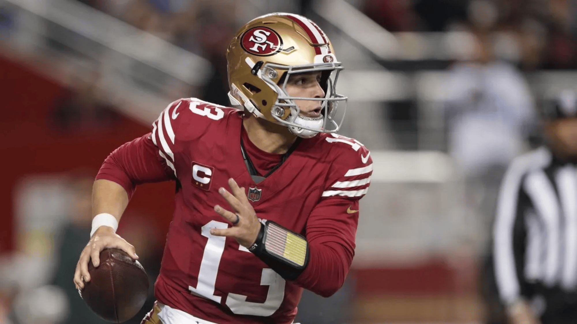 brock purdy in a red 49ers jersey and gold helmet prepares to throw a pass during a game
