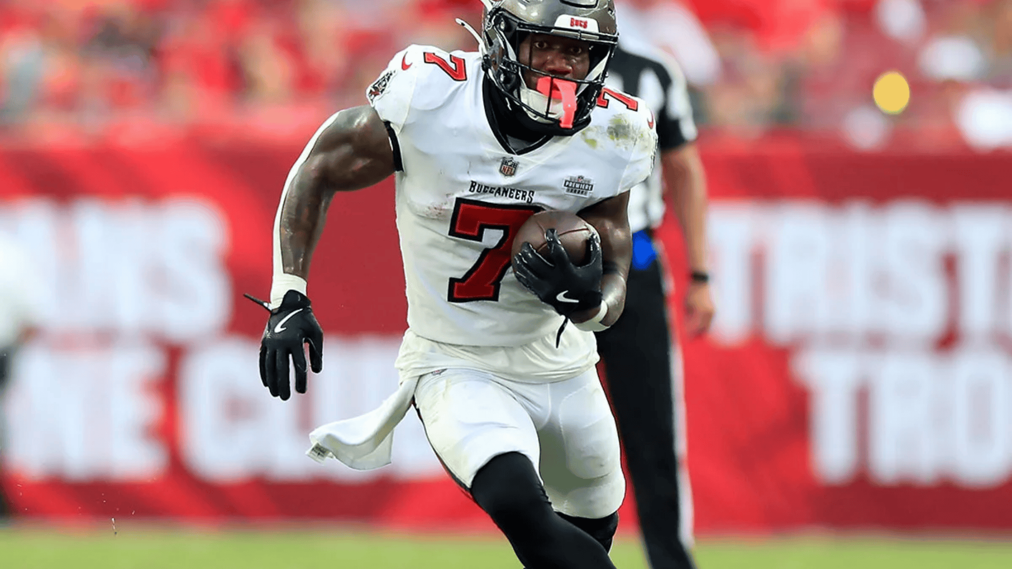 bucky irving in a white tampa bay buccaneers uniform runs with a football on a grassy field