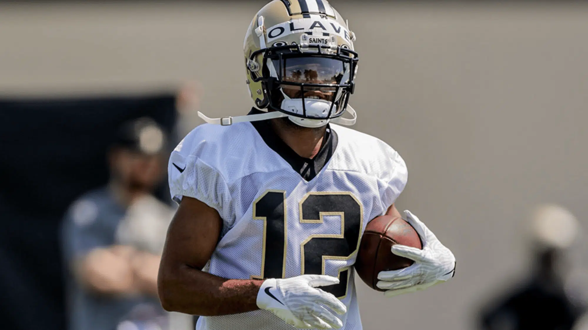 chris olave in a white jersey with the number 12 holds a ball during practice