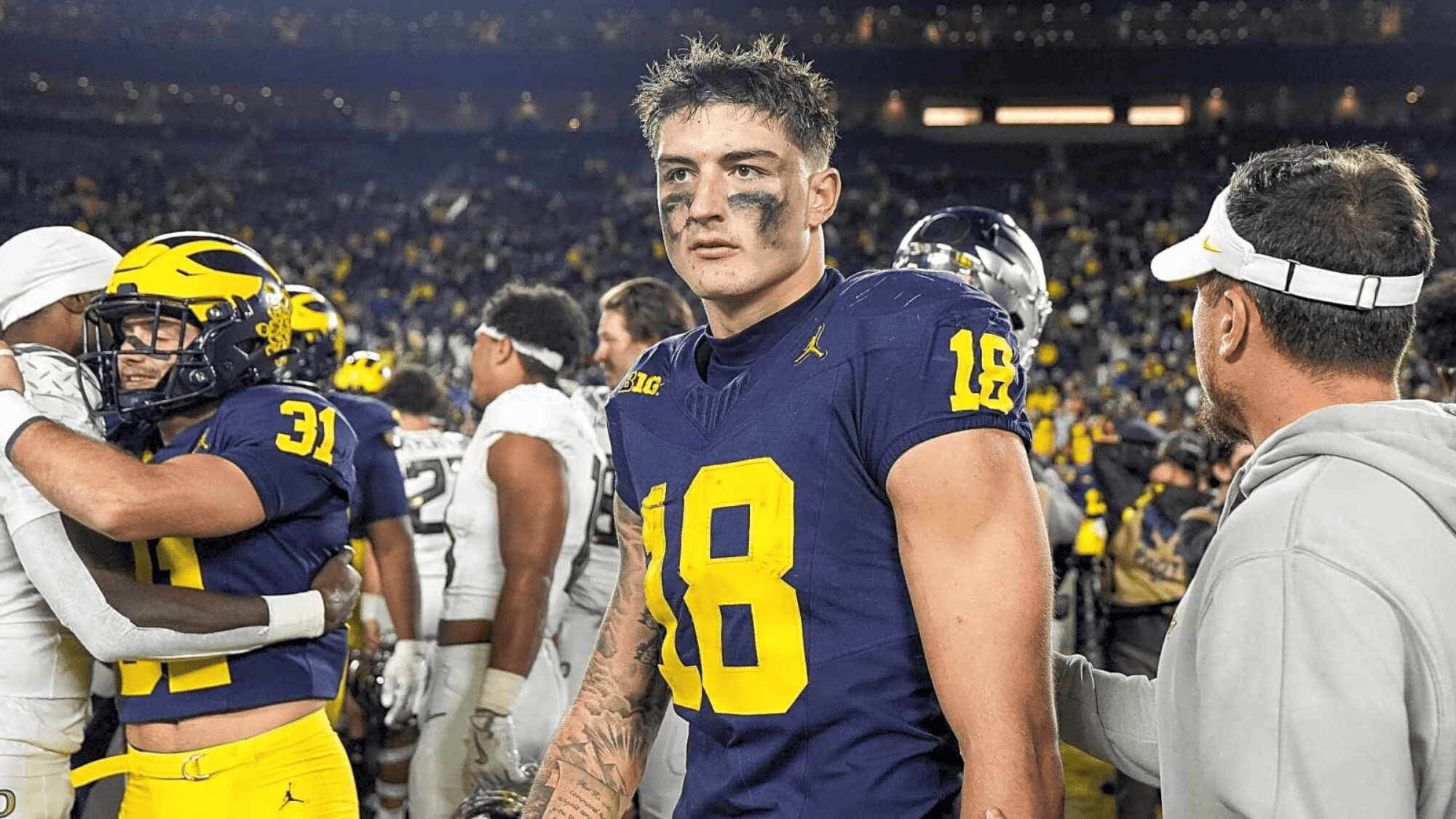colston loveland wearing a blue jersey with the number 18 and eye black stands on the field appearing focused