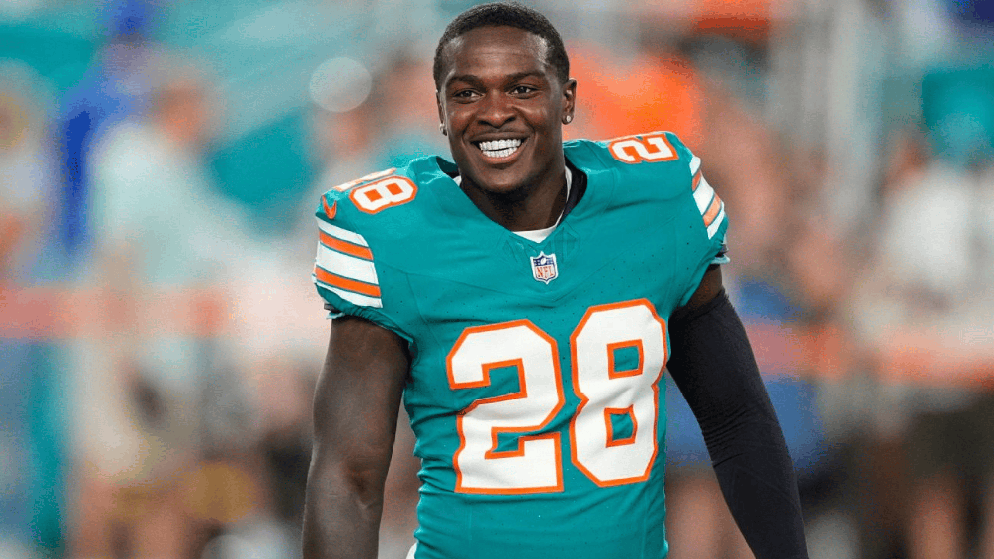 de'von achane in a teal jersey with number 28 standing on a field