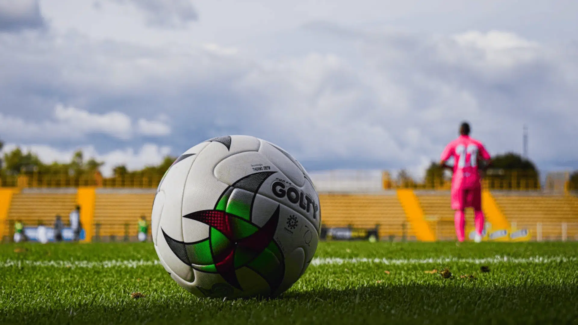 football on grass field with player in background and stadium seats behind