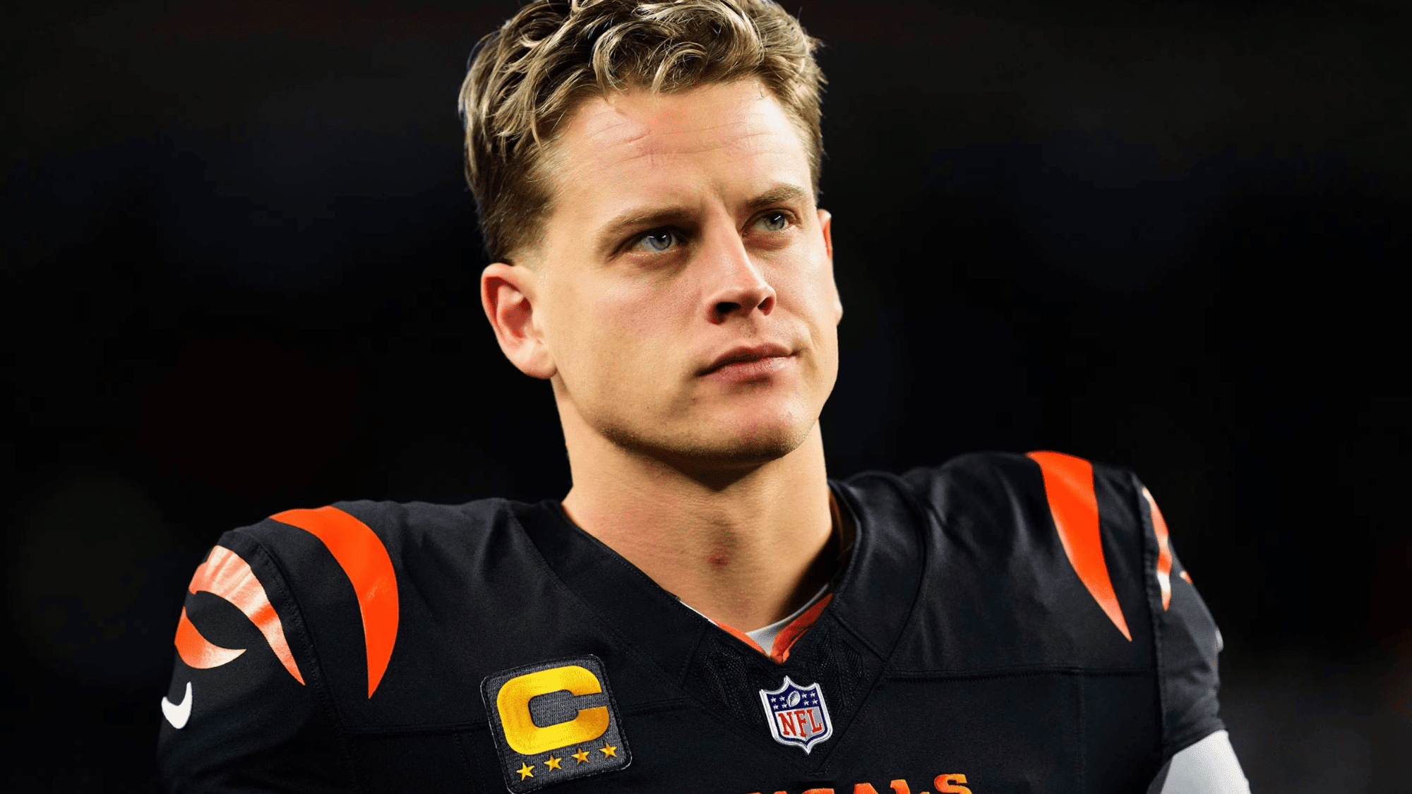 joe burrow in a black uniform with orange accents looks focused on the field