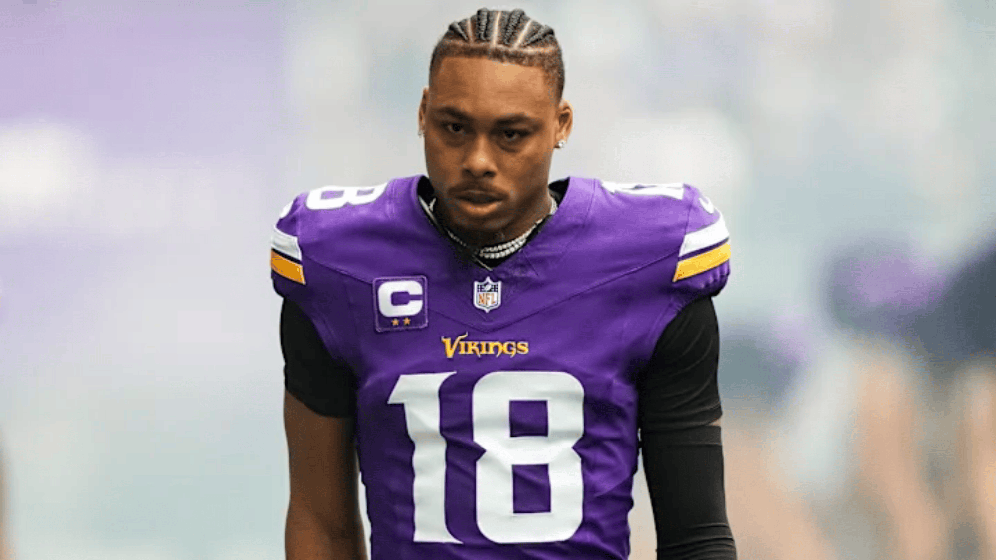 justin jefferson in a vikings jersey, number 18 with cornrow braids, looks focused