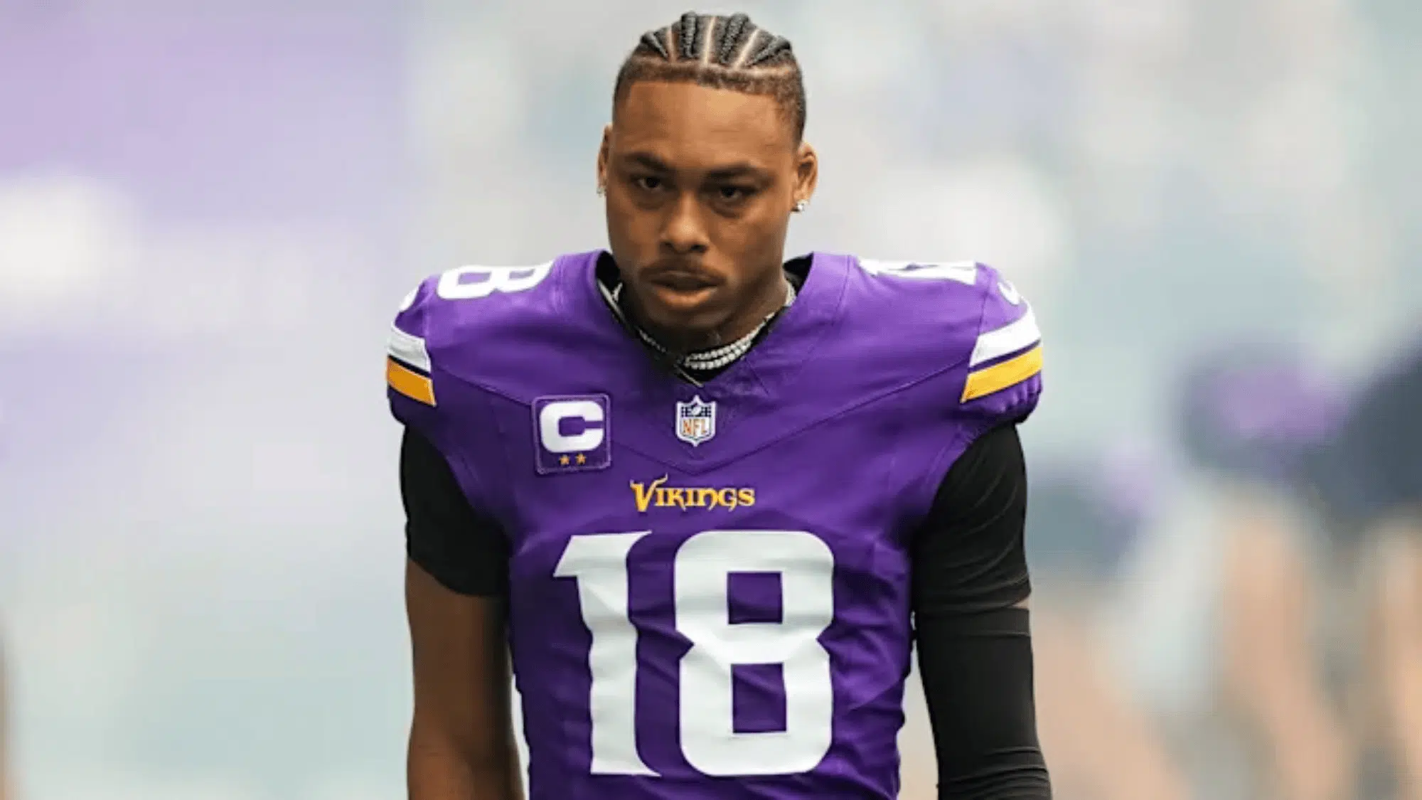 justin jefferson in a vikings jersey, number 18 with cornrow braids, looks focused