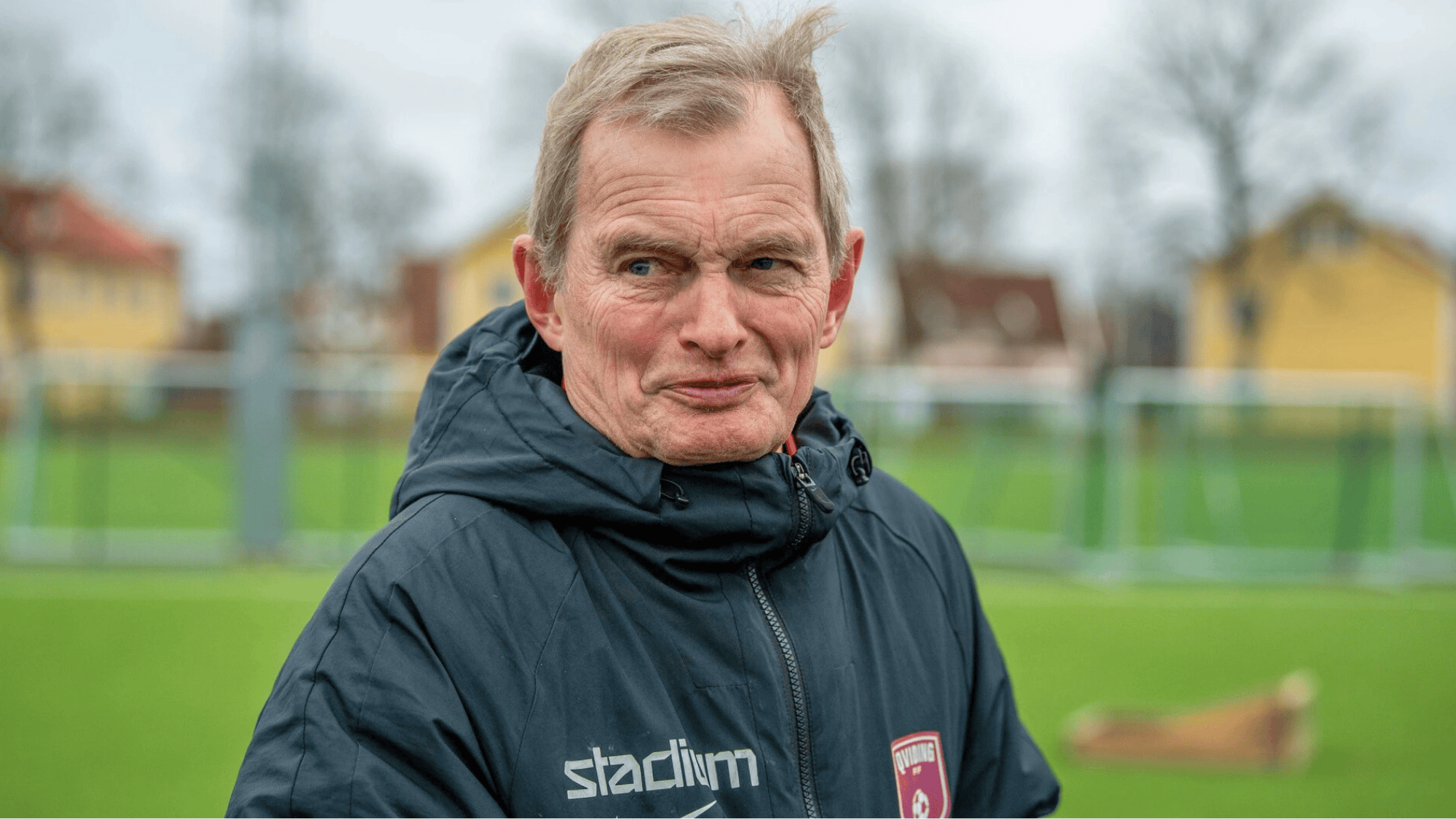 kjell pettersson in a dark jacket with the stadium logo and a red crest from the team Øvrevoll Hosle a Norwegian football club