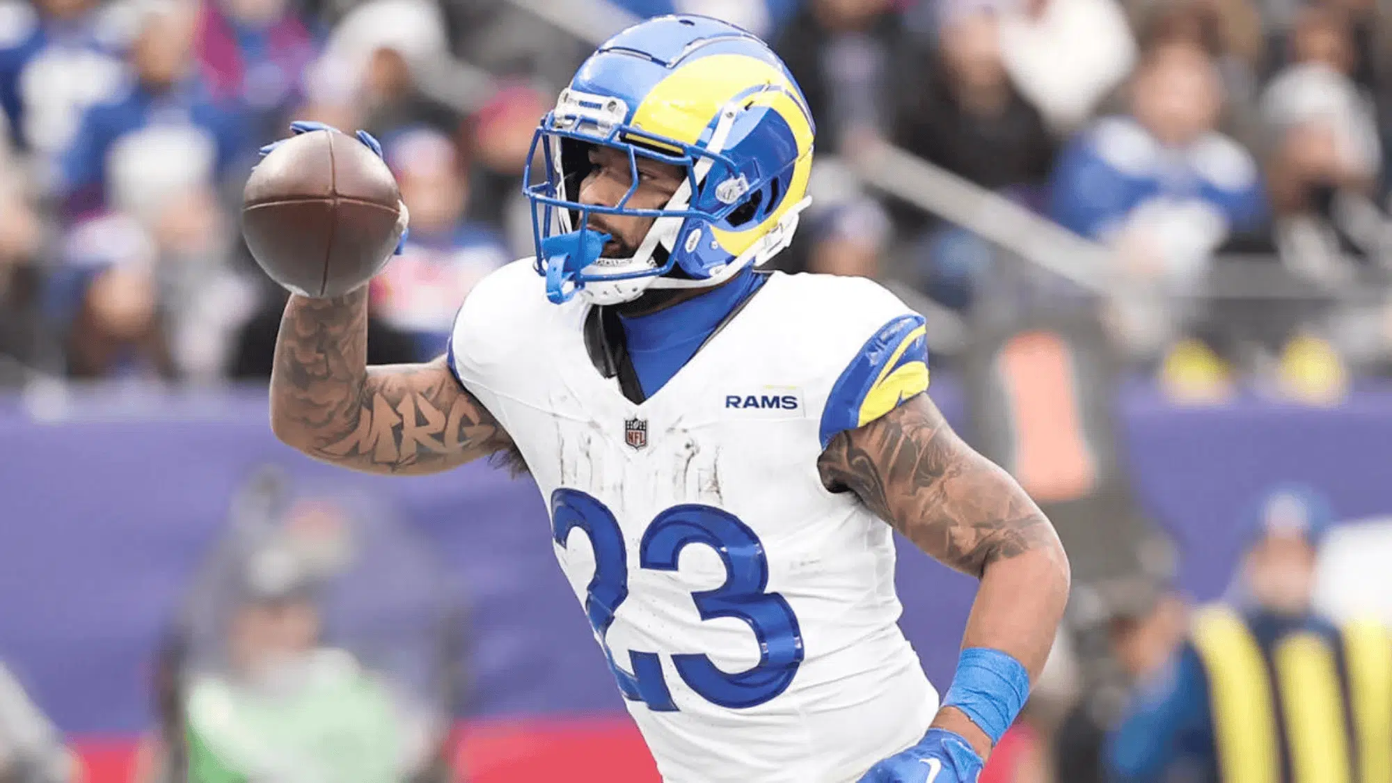 kyren williams in a white and blue Los angeles rams uniform runs while holding a football in his right hand