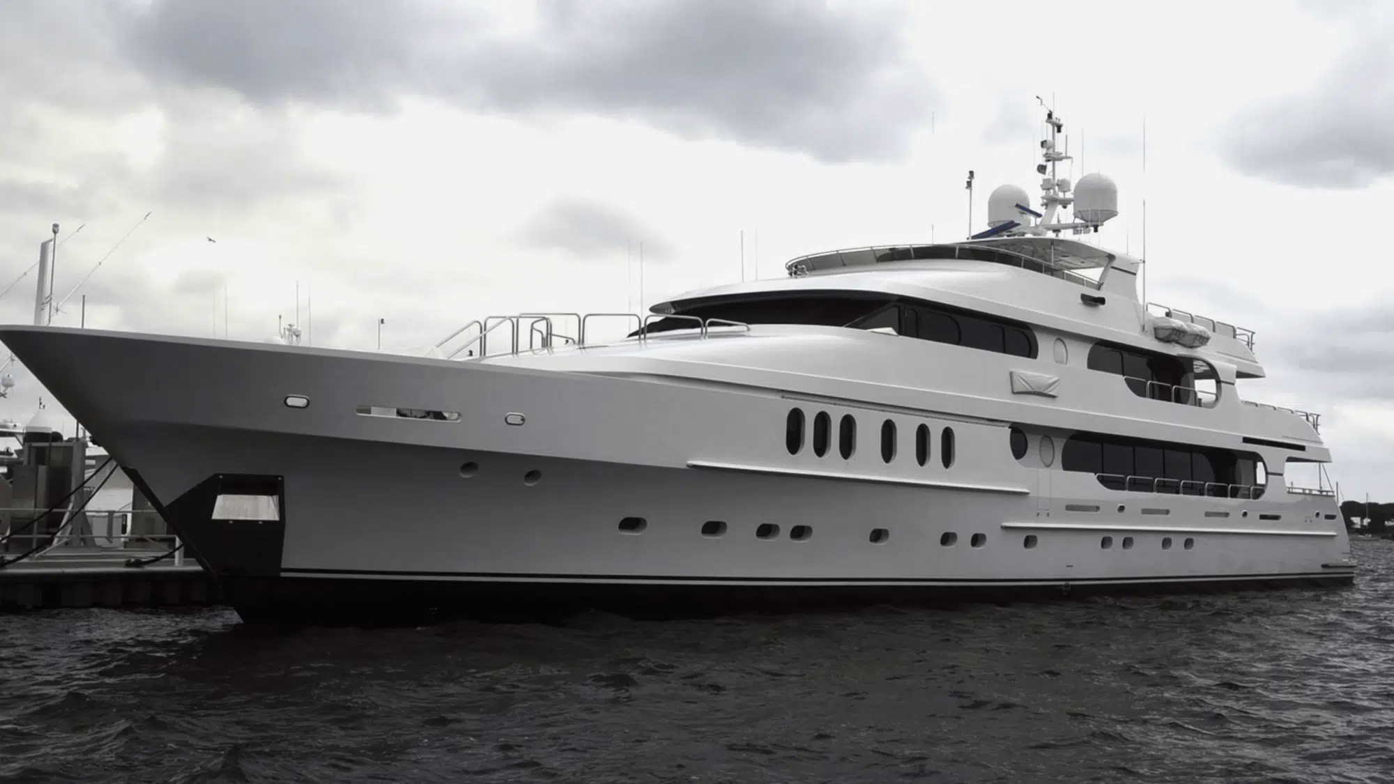 large white luxury yacht docked at marina with cloudy sky and calm water surrounding the vessel