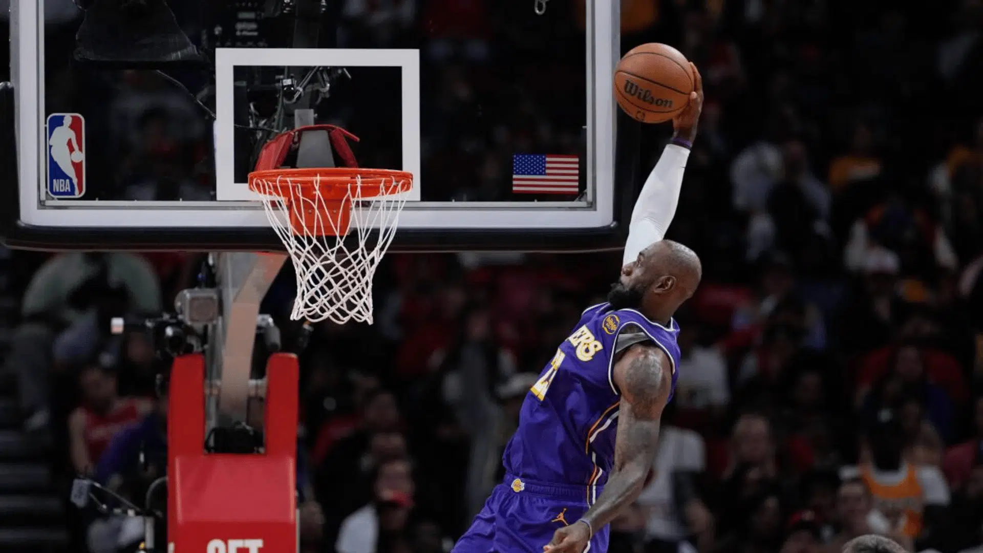 lebron james in purple jersey rises for a powerful dunk near the rim during a live game with crowd in background