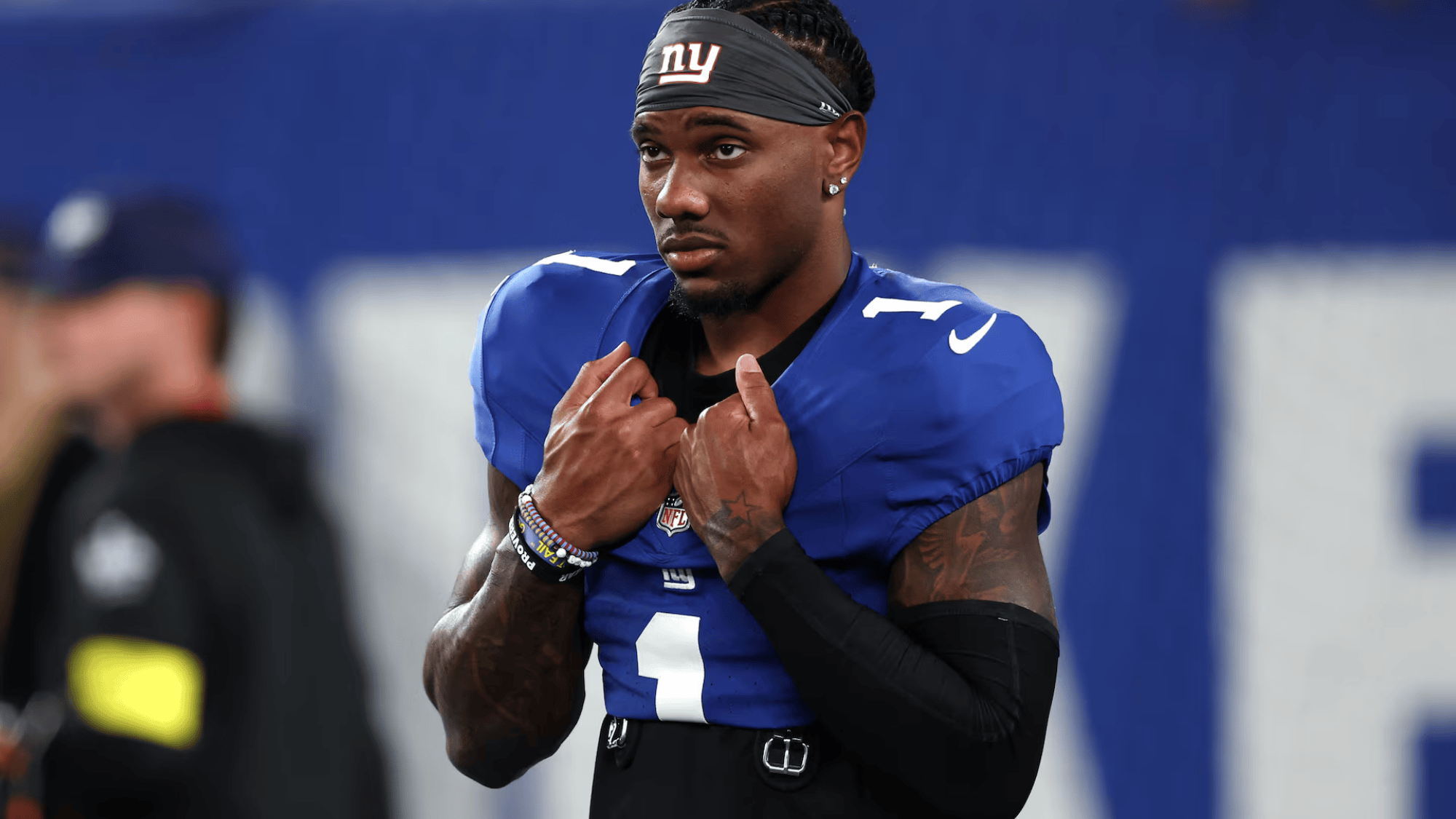 malik nabers in a blue jersey with number 1 wearing a headband and armbands, appears focused and thoughtful on the field