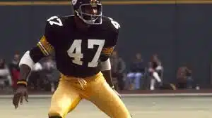 mel blount in a black jersey with number 47 and yellow pants is poised on a field focused and ready