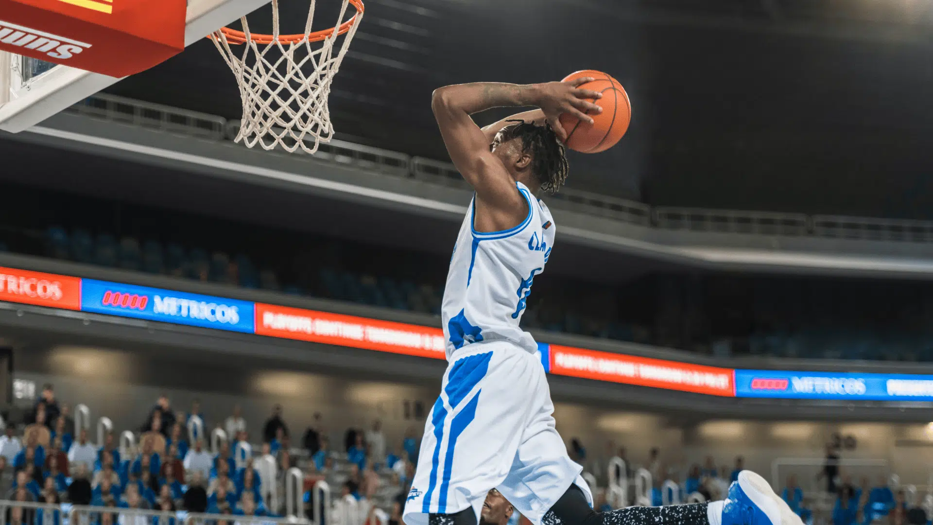 nba player jumping for a powerful dunk near the hoop during a live game with crowd in the background
