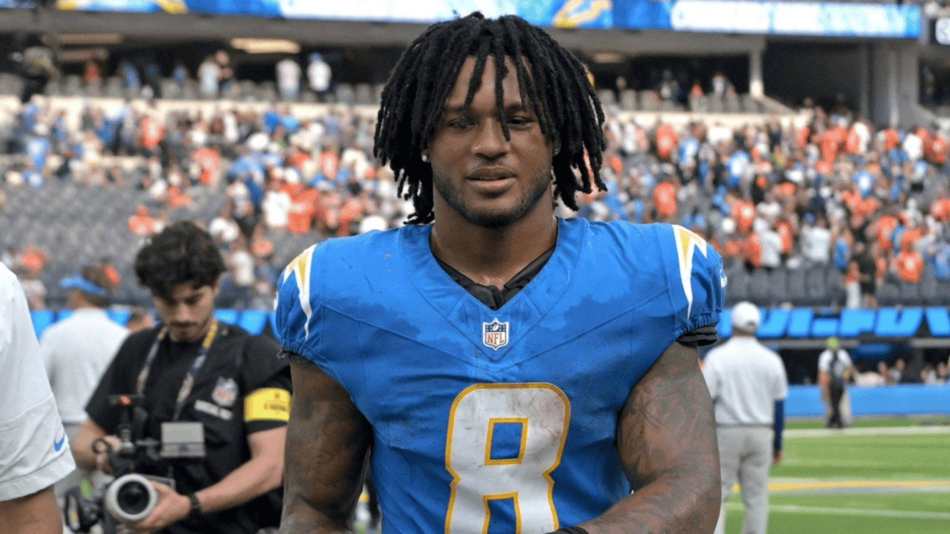 omarion hampton in a blue jersey with number 8 walks on a field holding a helmet