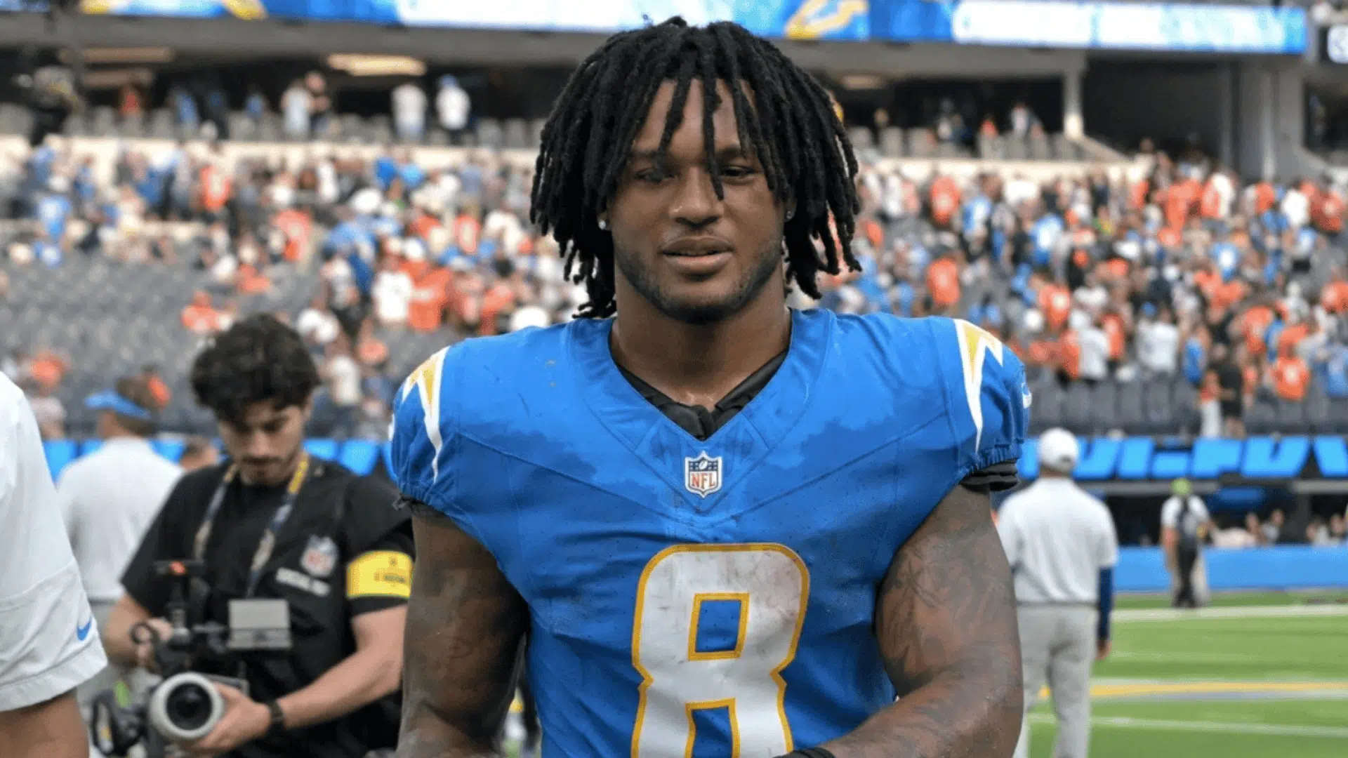 omarion hampton in a blue jersey with number 8 walks on a field holding a helmet