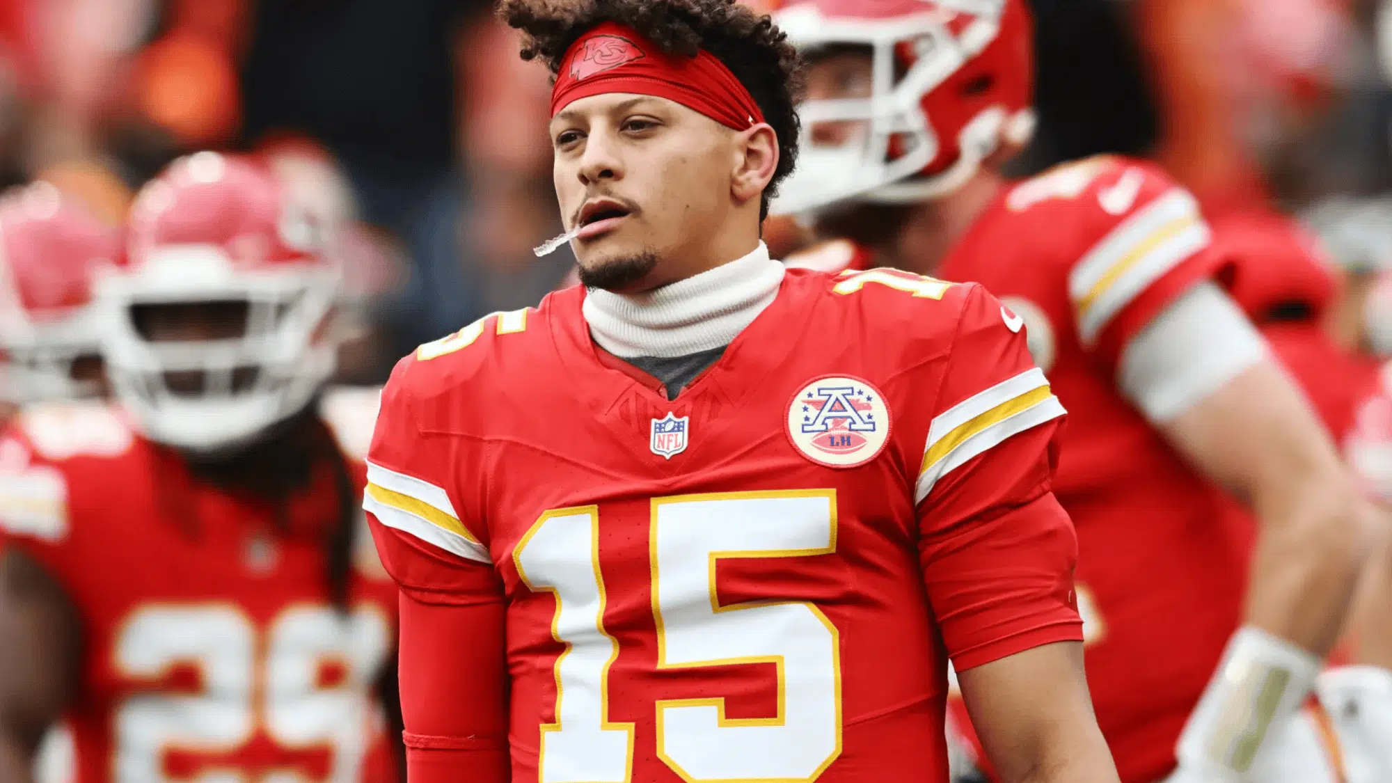 patrick mahomes in a red jersey with number 15 stands on the field with a focused expression