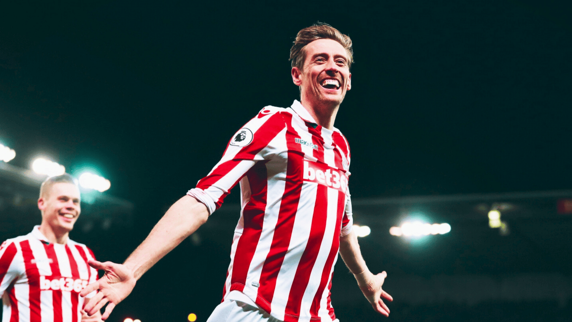 peter crouch is celebrating a goal in a red and white striped kit for Stoke City in the Premier League