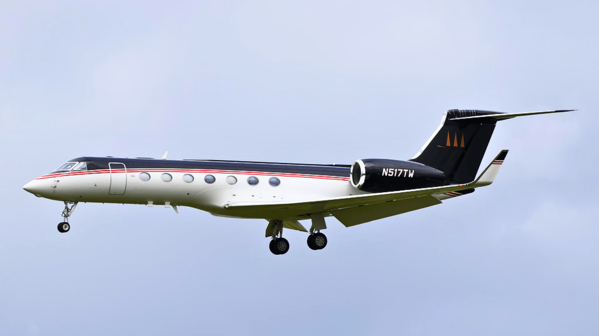 private jet flying in clear sky with landing gear down and sleek white and black body