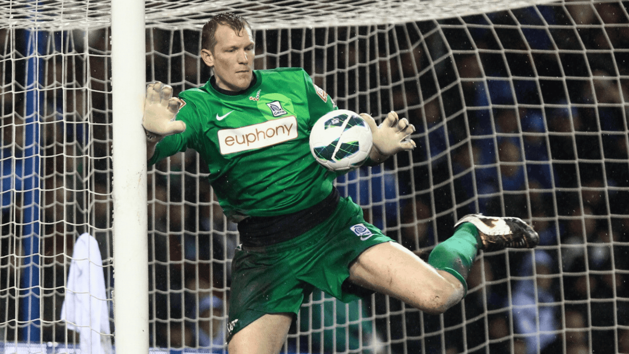 the image shows goalkeeper kristof van hout in a green kit making a save during a match with the ball in mid air