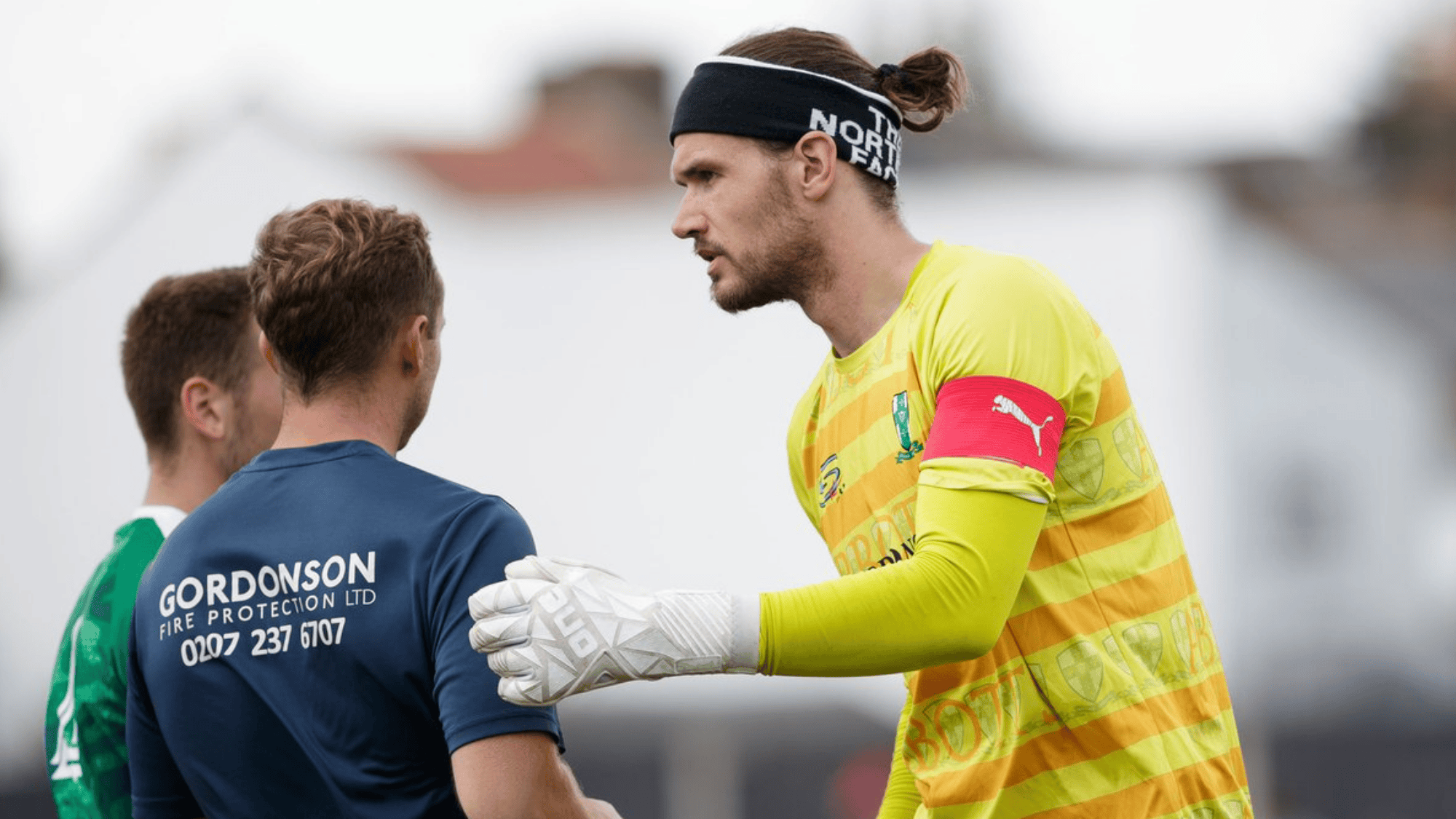 the image shows simon bloch jørgensen in yellow and green kit wearing a headband shaking hands with teammates
