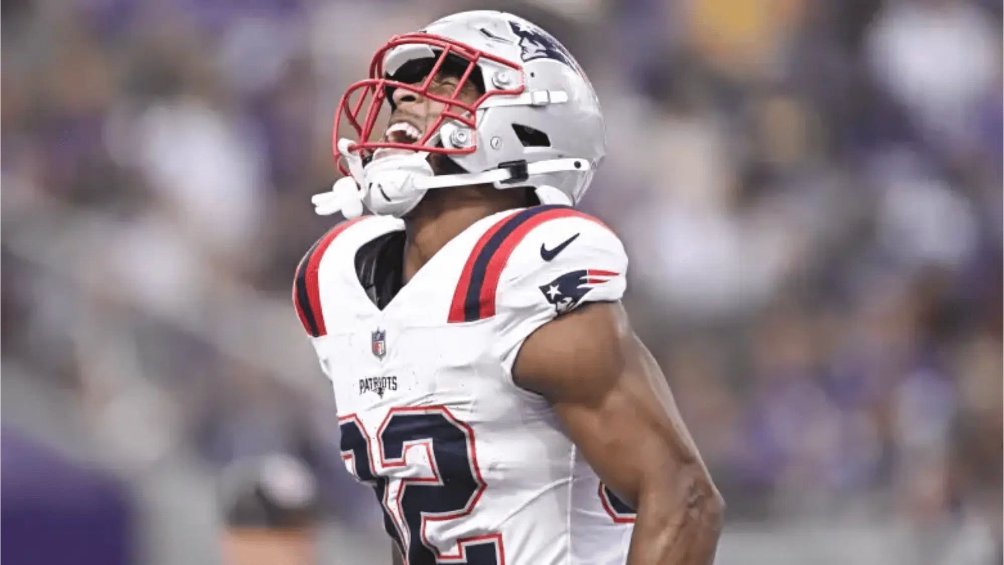 treveyon henderson in a white uniform and helmet with red accents shouting in celebration on the field conveying determination and energy