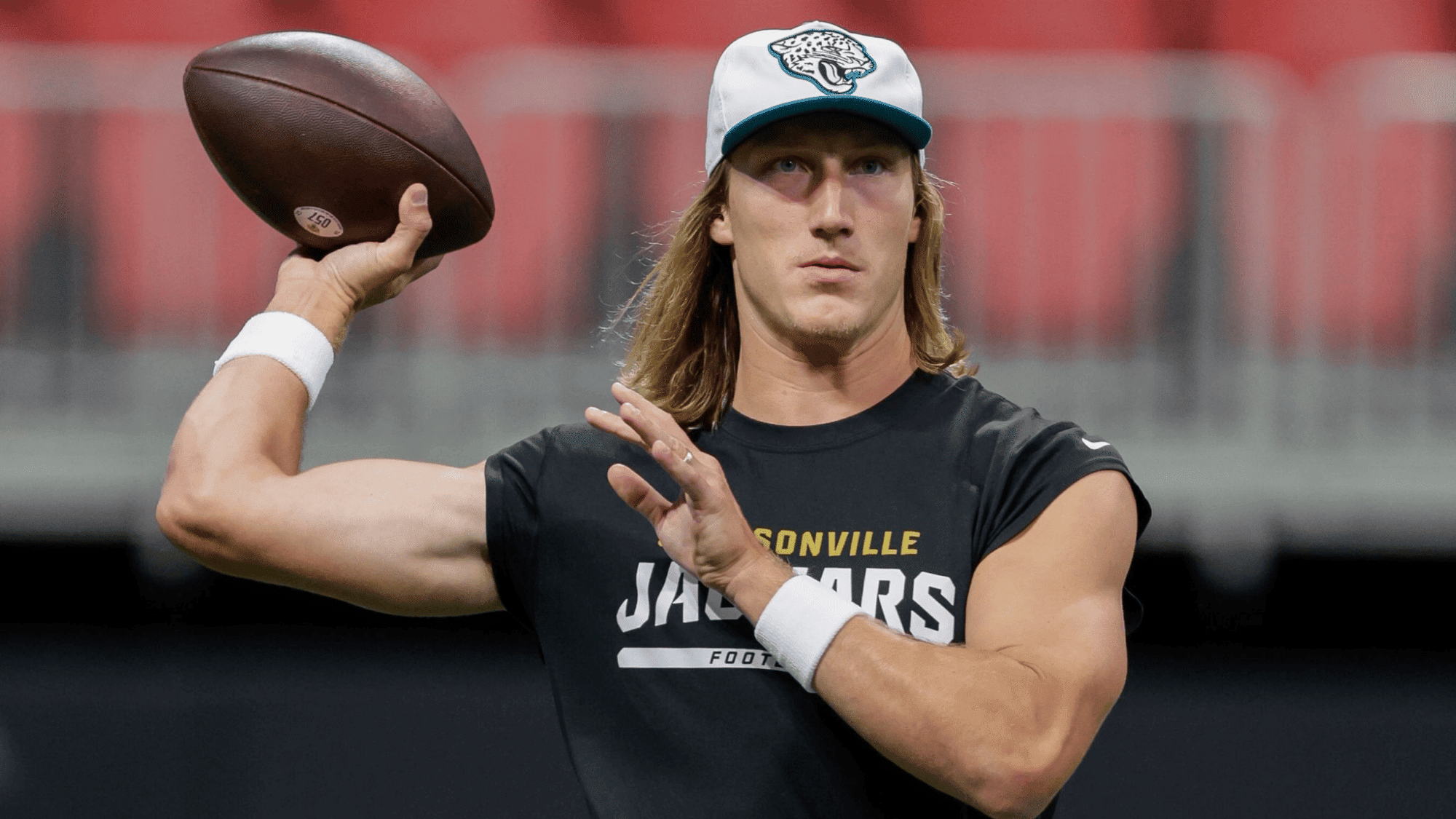 trevor lawrence in a jacksonville jaguars shirt and cap holds a football poised to throw