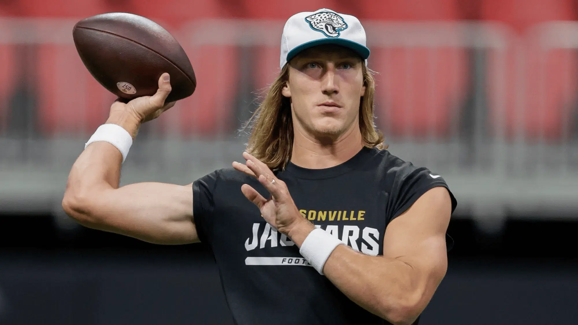 trevor lawrence in a jacksonville jaguars shirt and cap holds a football poised to throw