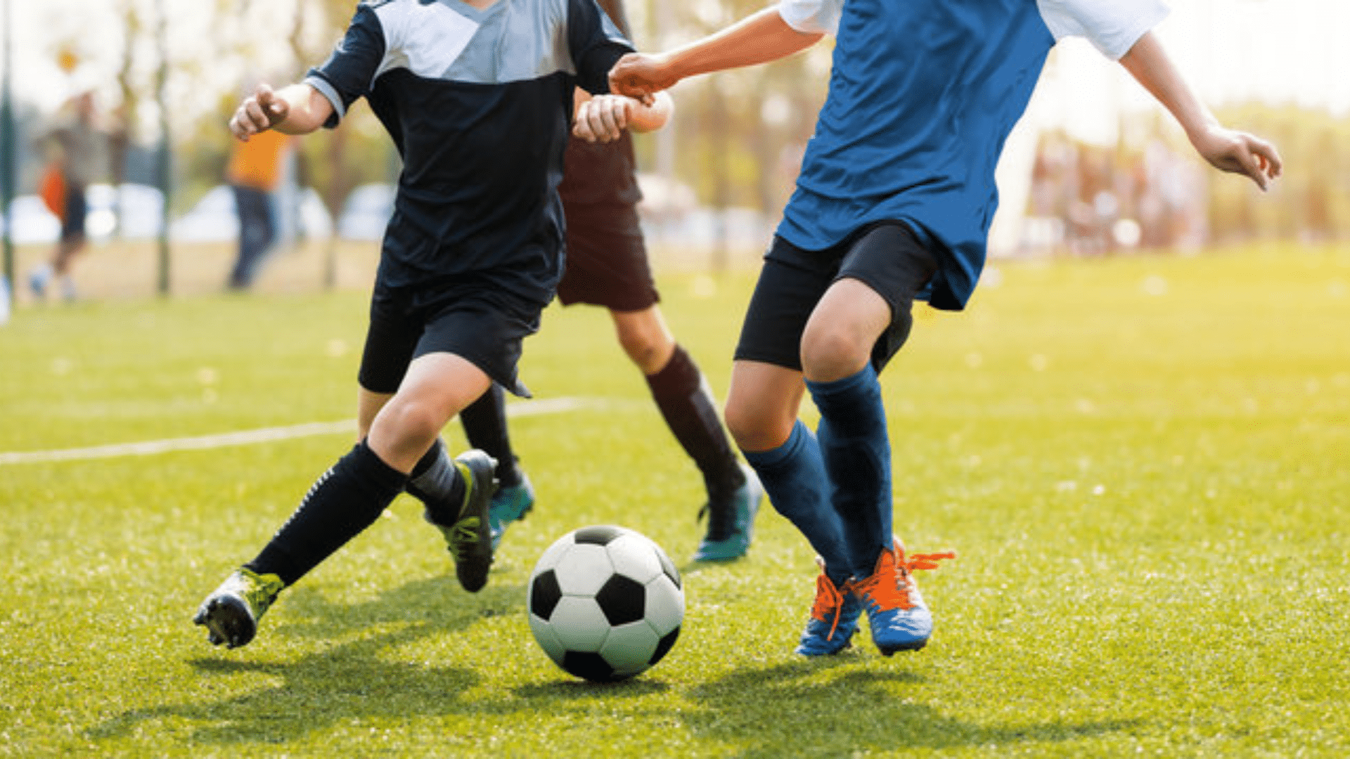 two youth soccer players competing for the ball on a sunny field with green grass and blurred spectators in background