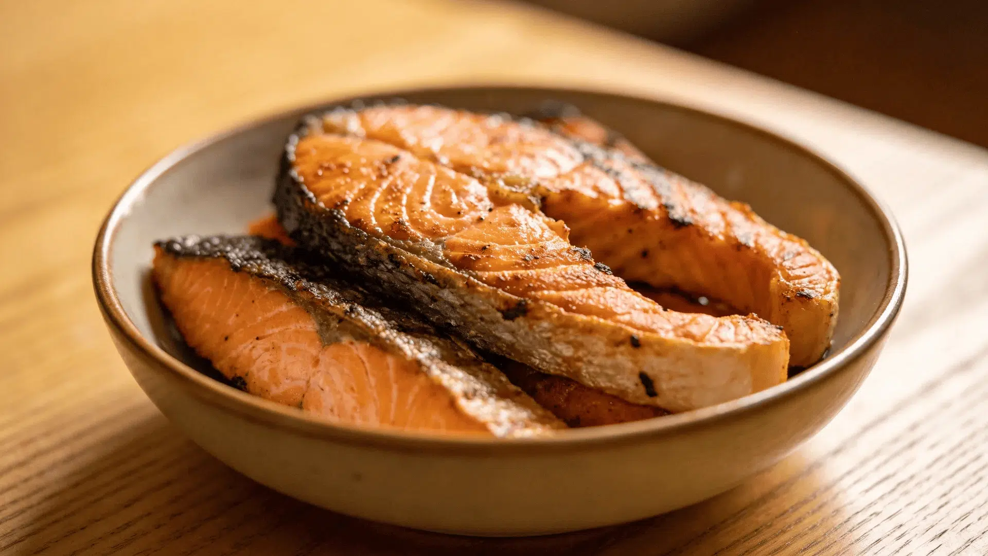 a plate holding grilled salmon slices with crispy skin placed on a wooden table in warm lighting