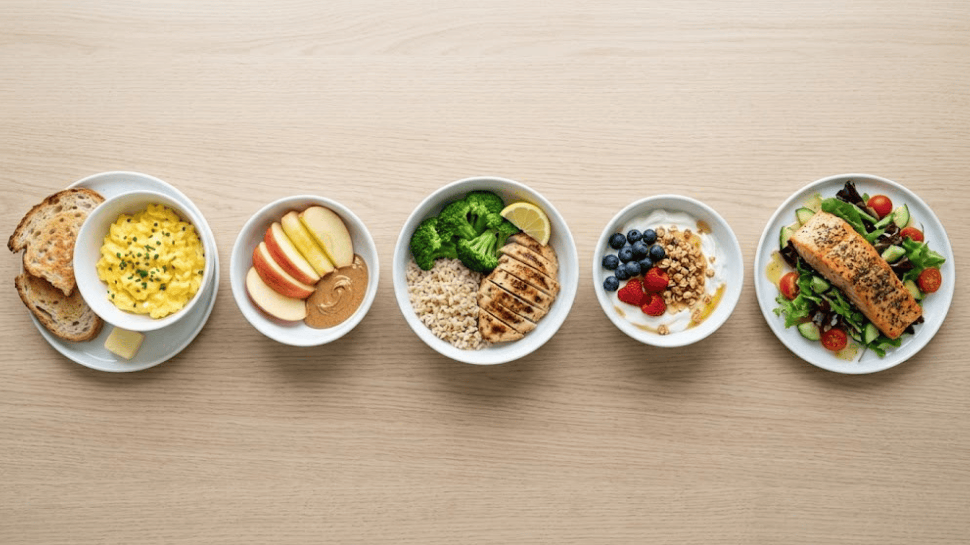 a row of bowls with scrambled eggs toast apple slices peanut butter grilled chicken broccoli rice yogurt berries and salmon salad