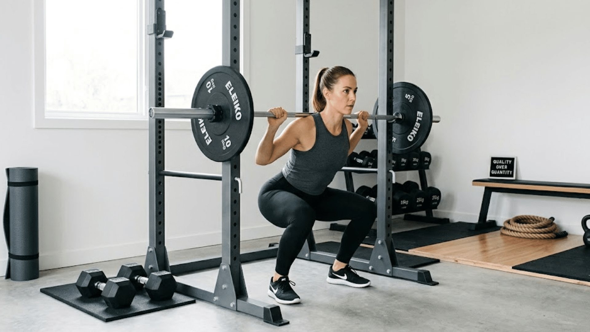 a woman performing a barbell squat in a home gym with weight rack dumbbells and exercise equipment around her