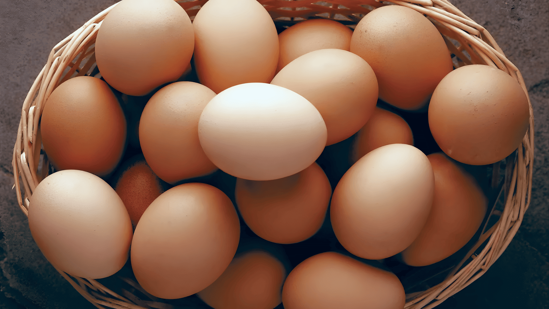 a woven basket filled with brown and white eggs arranged closely together on a textured surface