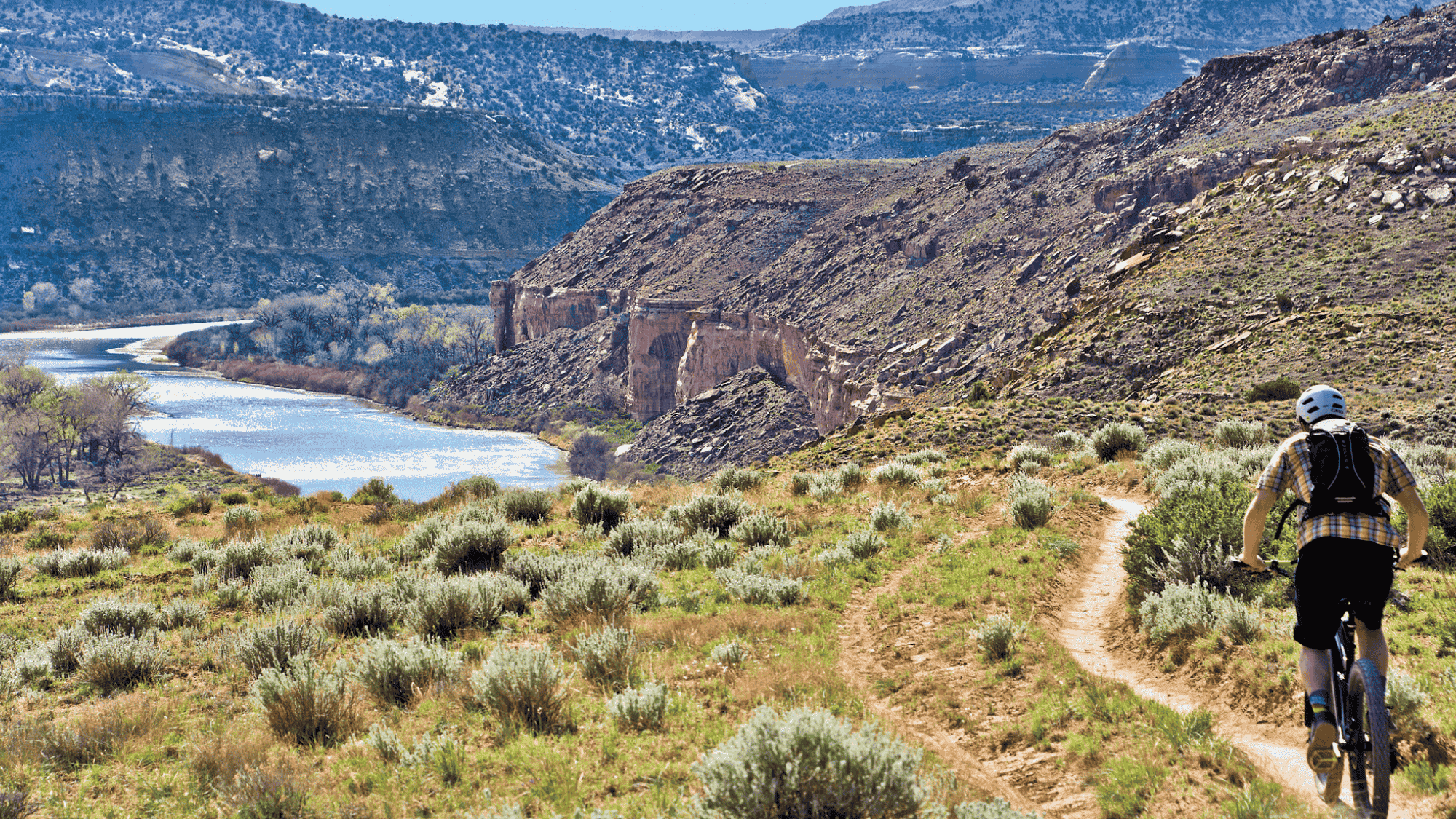 biker riding on trail near river in colorado fruita trails with canyon views and dry hills around