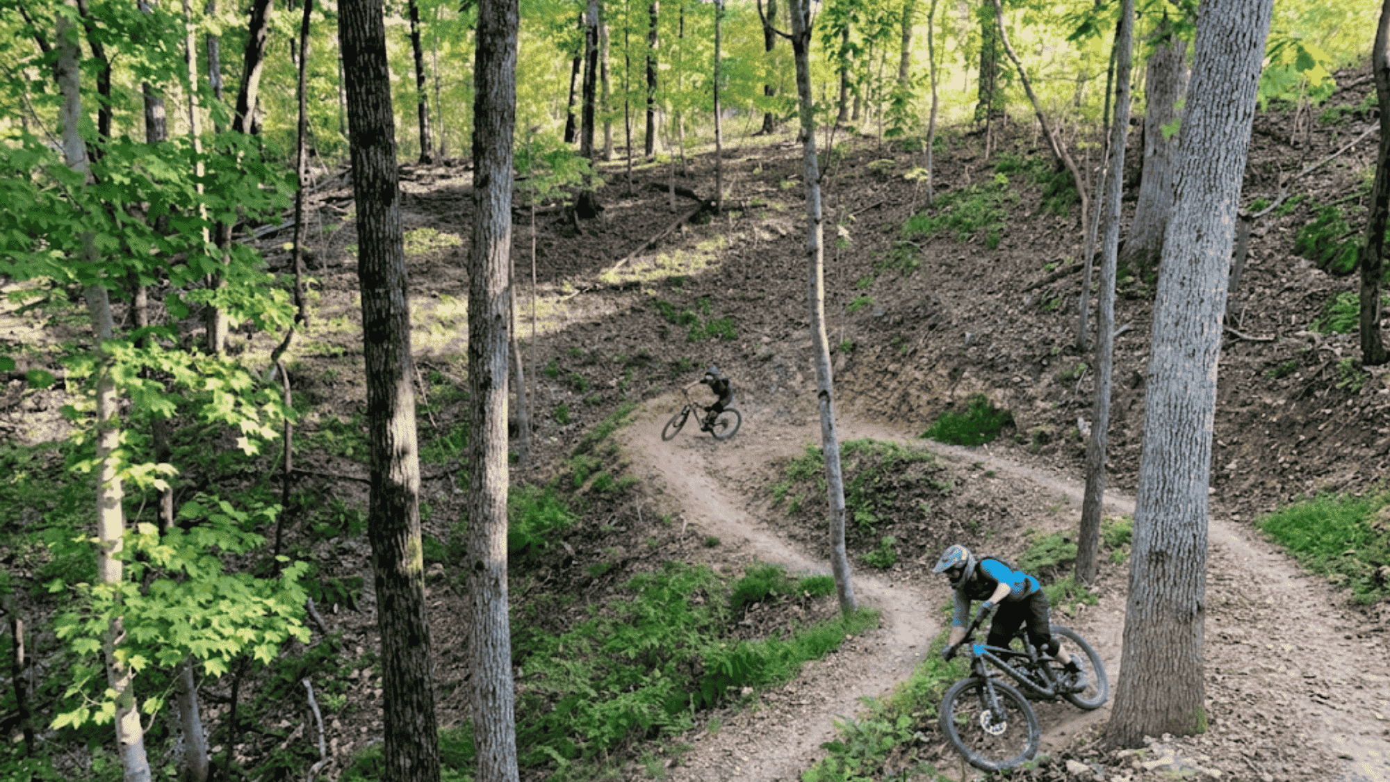 biker riding on winding dirt trail in arkansas bentonville trail system through green forest trees
