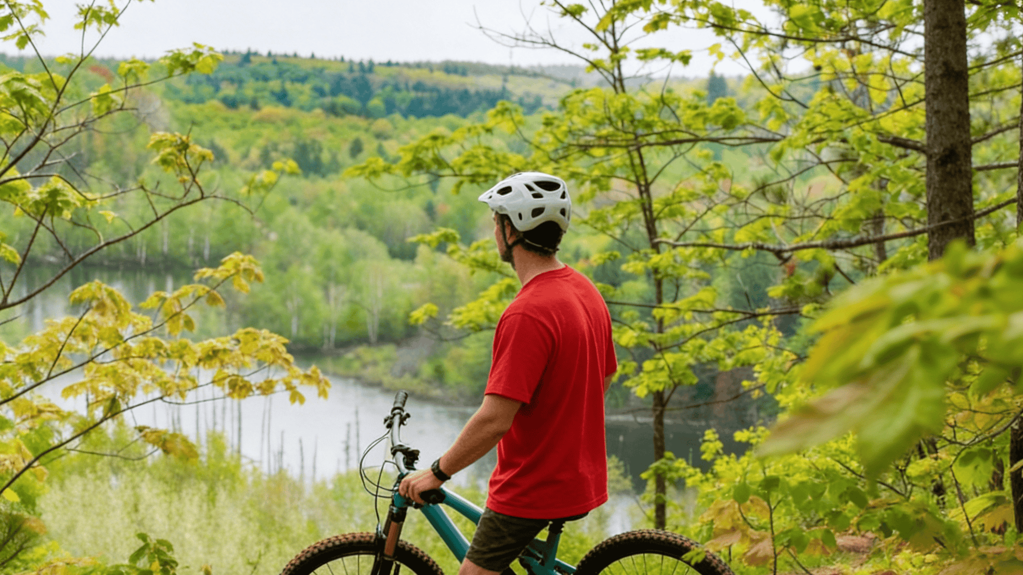 biker standing with bike near lake in forest best mountain biking trails with green trees and view