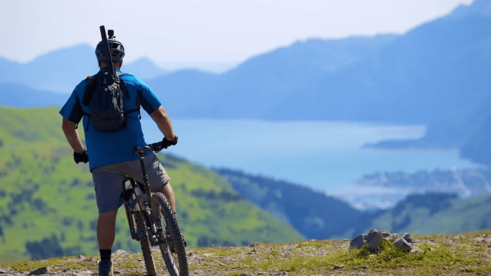 biker standing with bike on hill in alaska anchorage trails with lake mountains and wide view