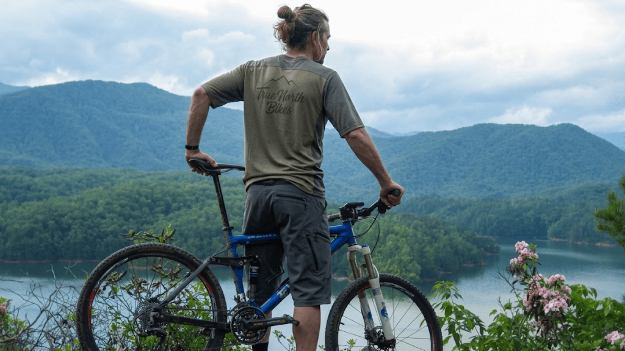 biker standing with bike overlooking lake and mountains in north carolina tsali trails scenic view