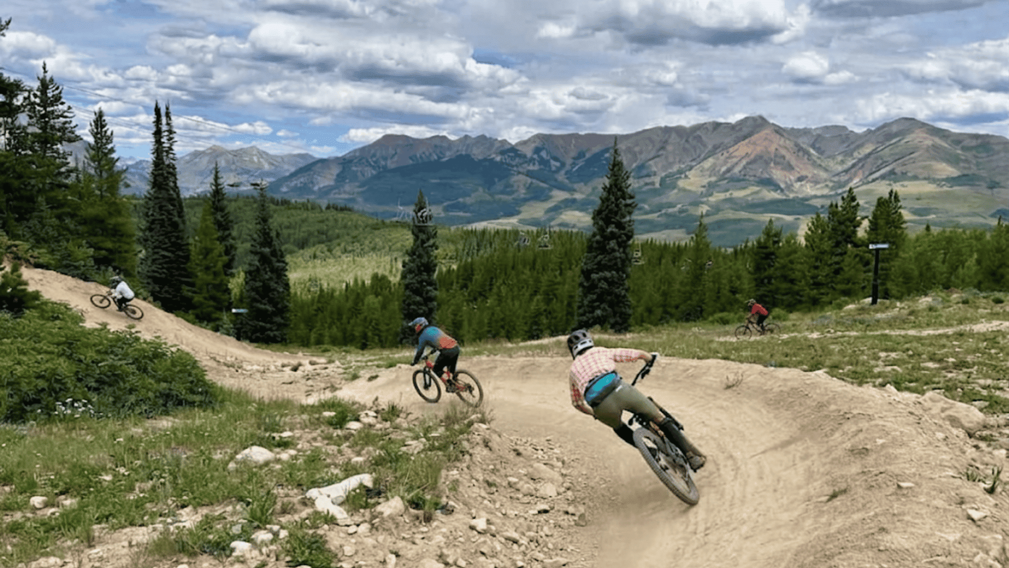 bikers riding on dirt trail in colorado crested butte trails with mountains trees and wide view