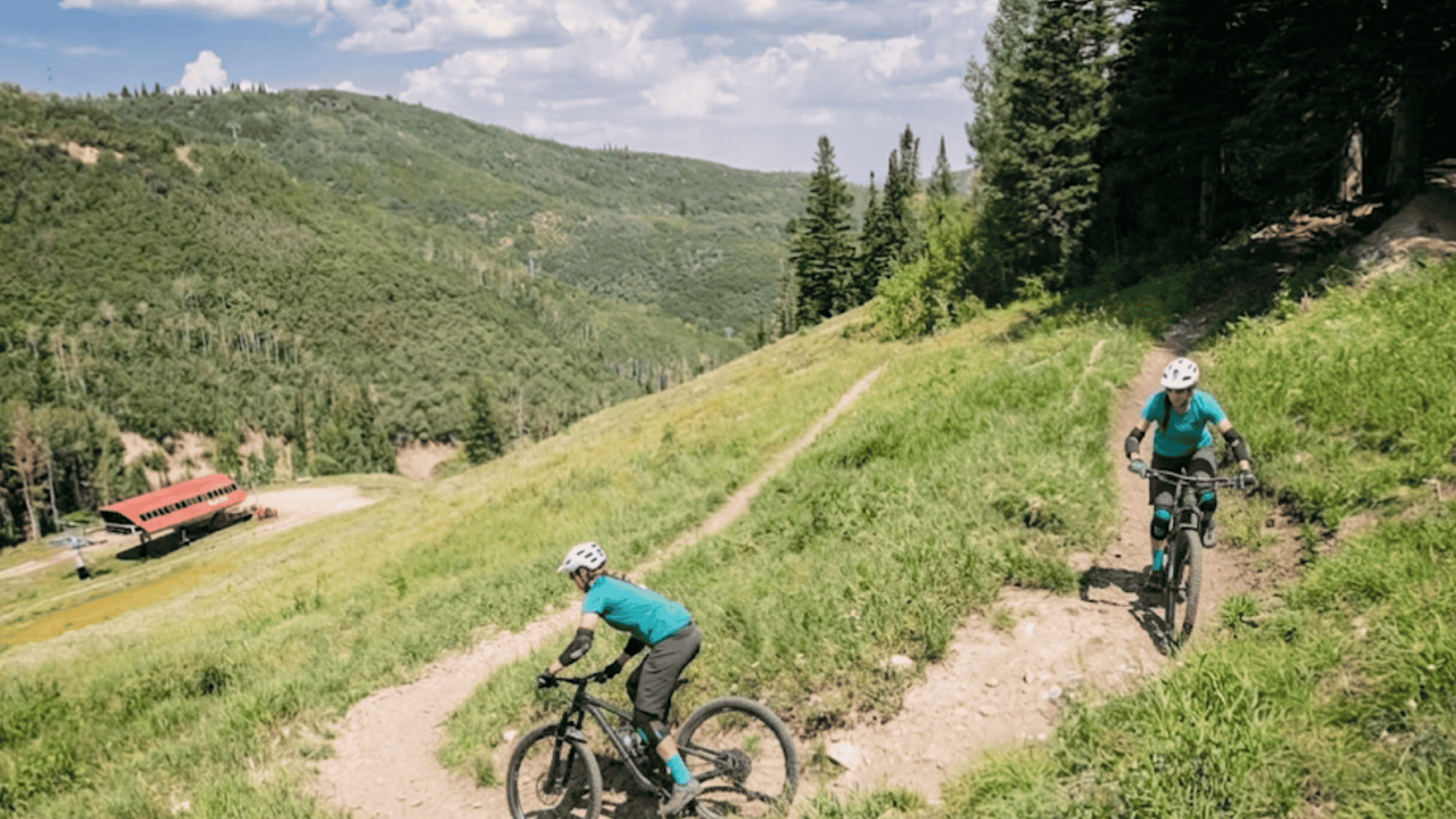 bikers riding on dirt trail in utah park city trail system with green hills and mountain views