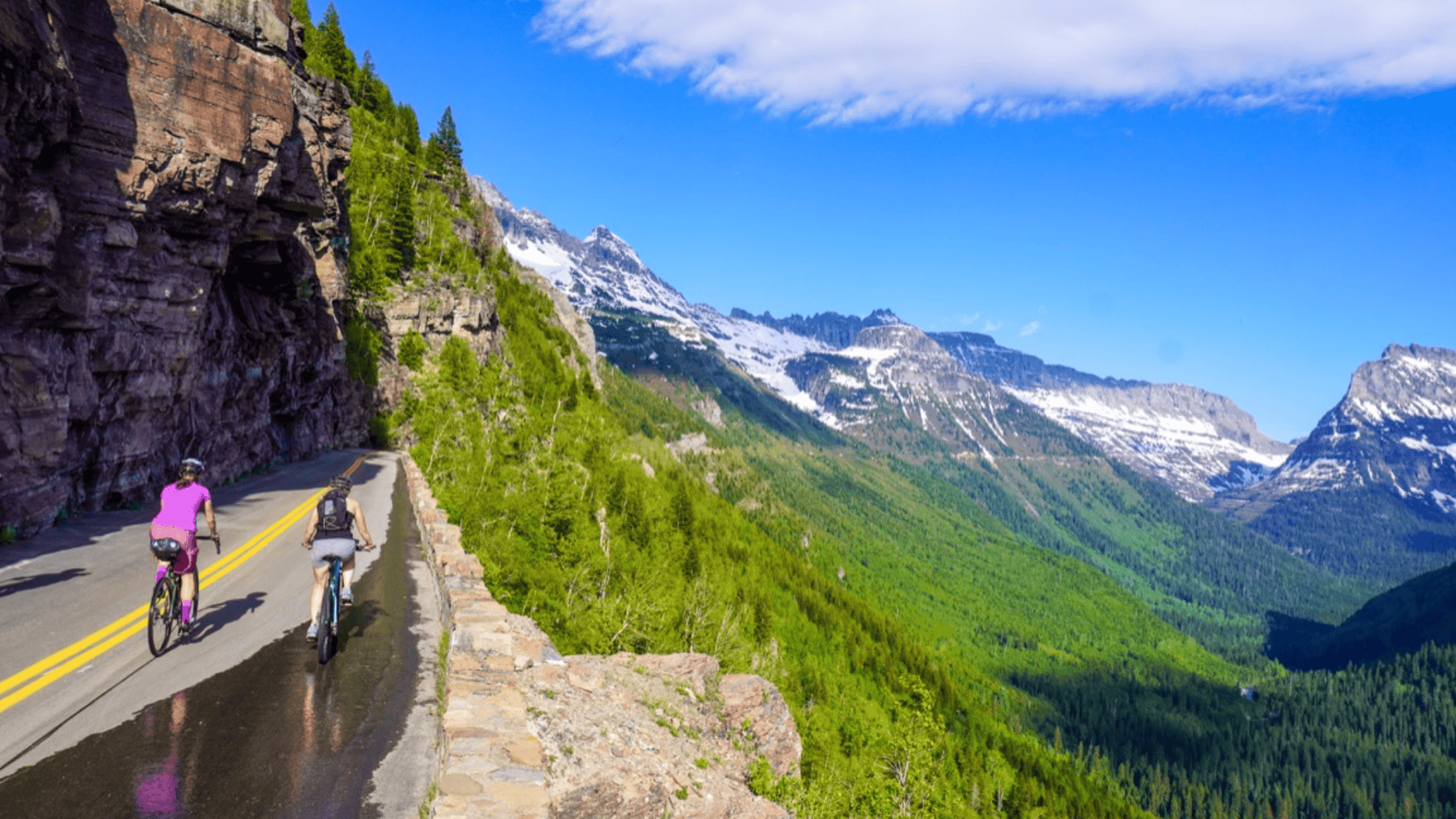 bikers riding on mountain road in montana whitefish trail with cliffs trees and snowy peaks view
