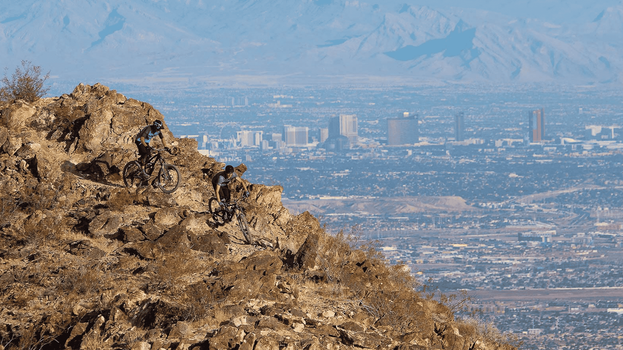 bikers riding on rocky mountain trail in nevada bootleg canyon with desert hills and city view