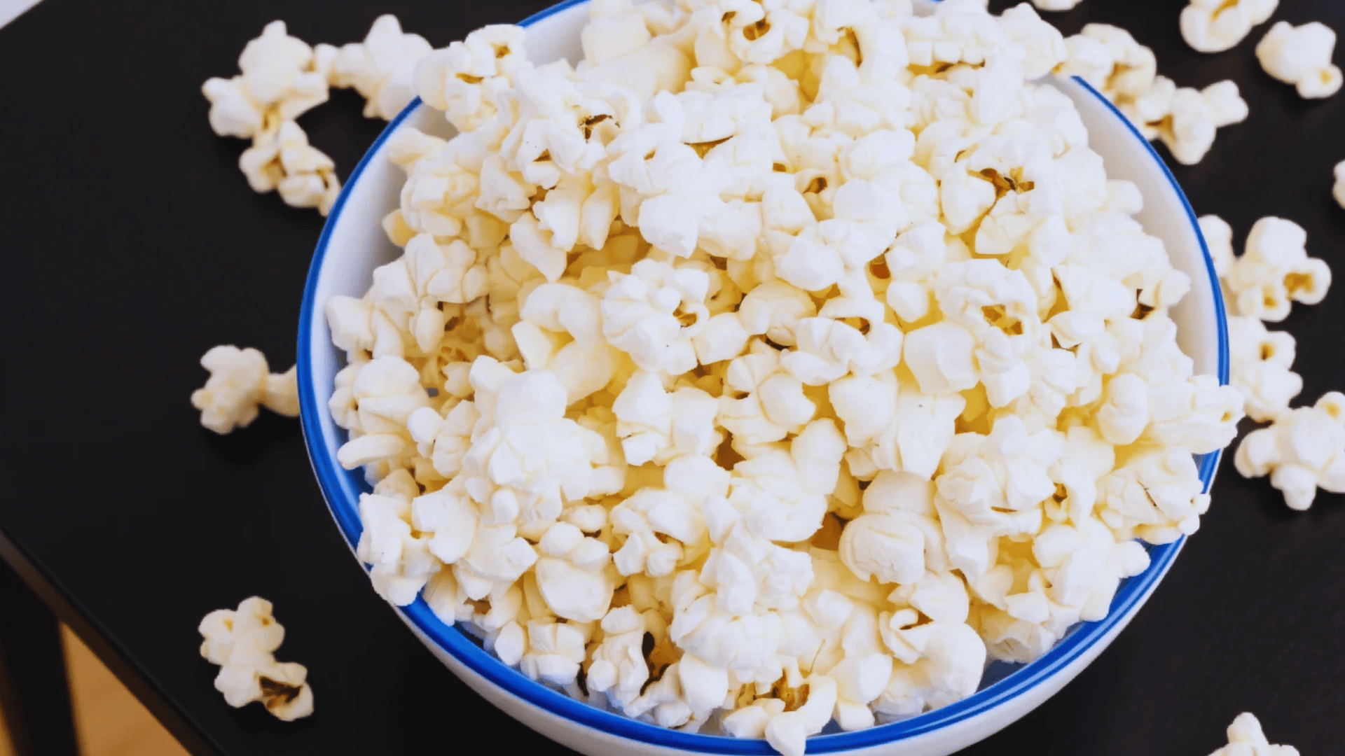 bowl of plain popcorn on table with scattered kernels
