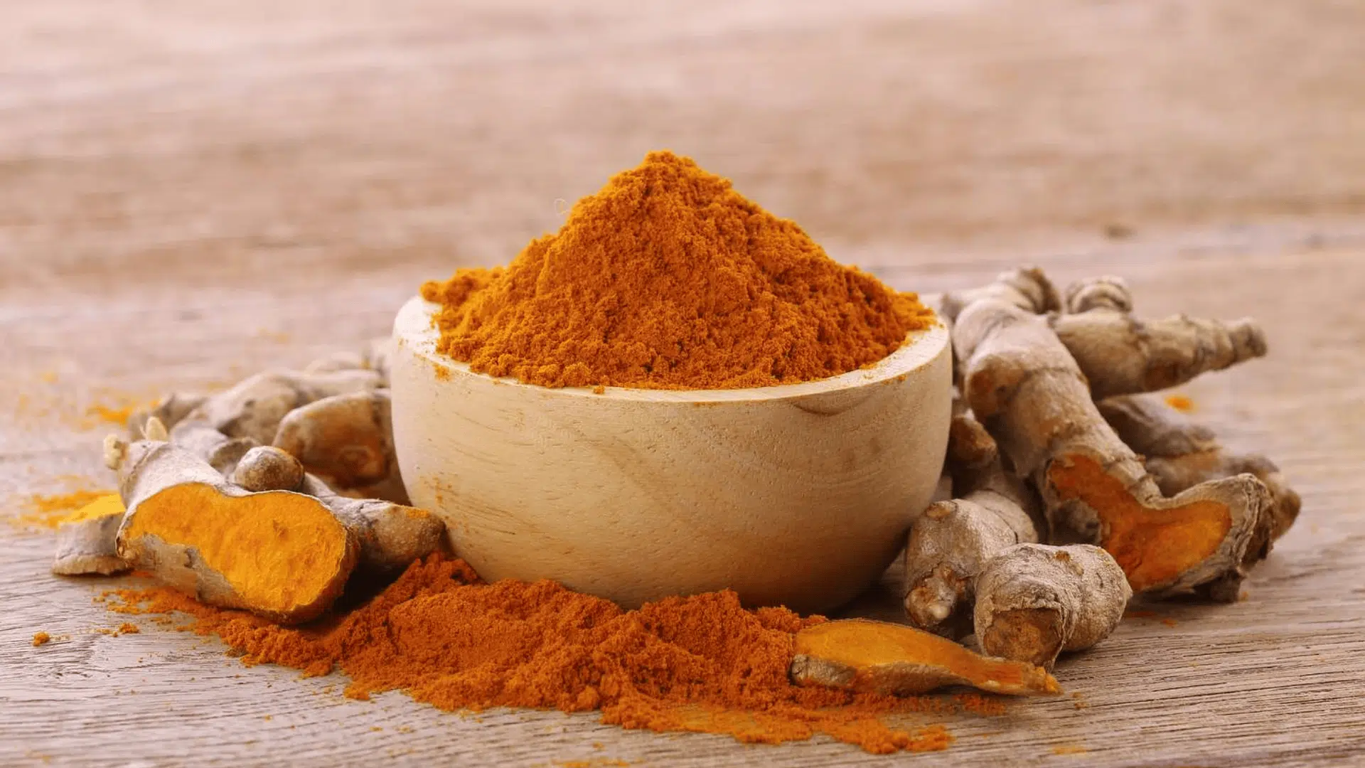 bowl of turmeric powder with fresh turmeric roots on wooden table showing spice texture and color