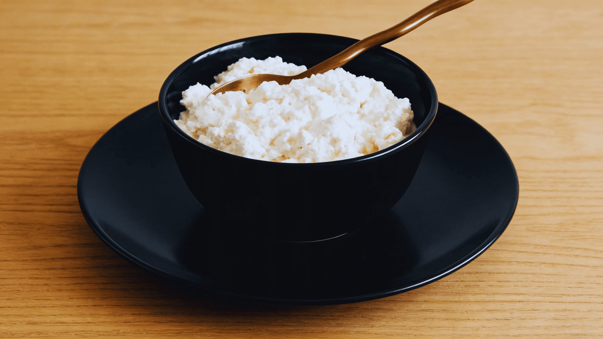 cottage cheese in a black bowl with a spoon on wooden table