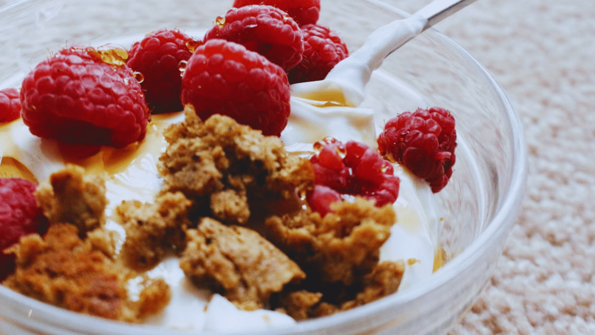greek yogurt with raspberries honey and granola in a glass bowl