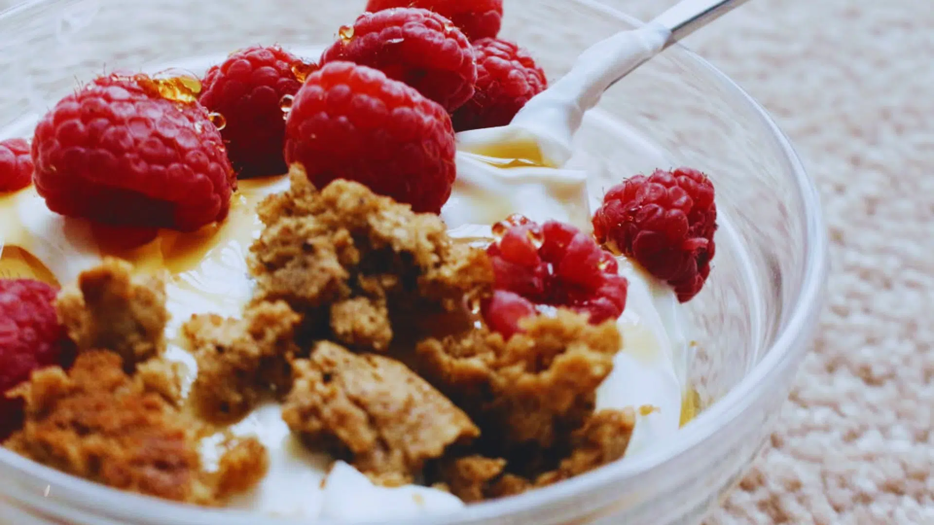 greek yogurt with raspberries honey and granola in a glass bowl